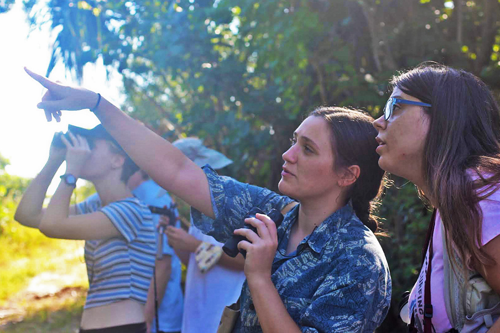 Students pointing into the woods while holding binoculars