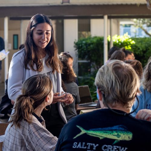 Professor standing by table of students seated outside