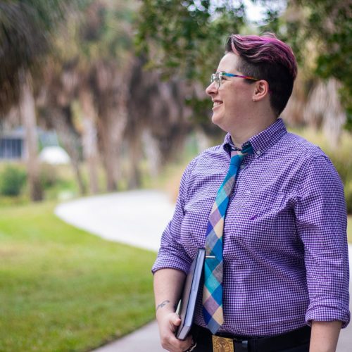 Professor with purple hair and tie on sidewalk on campus