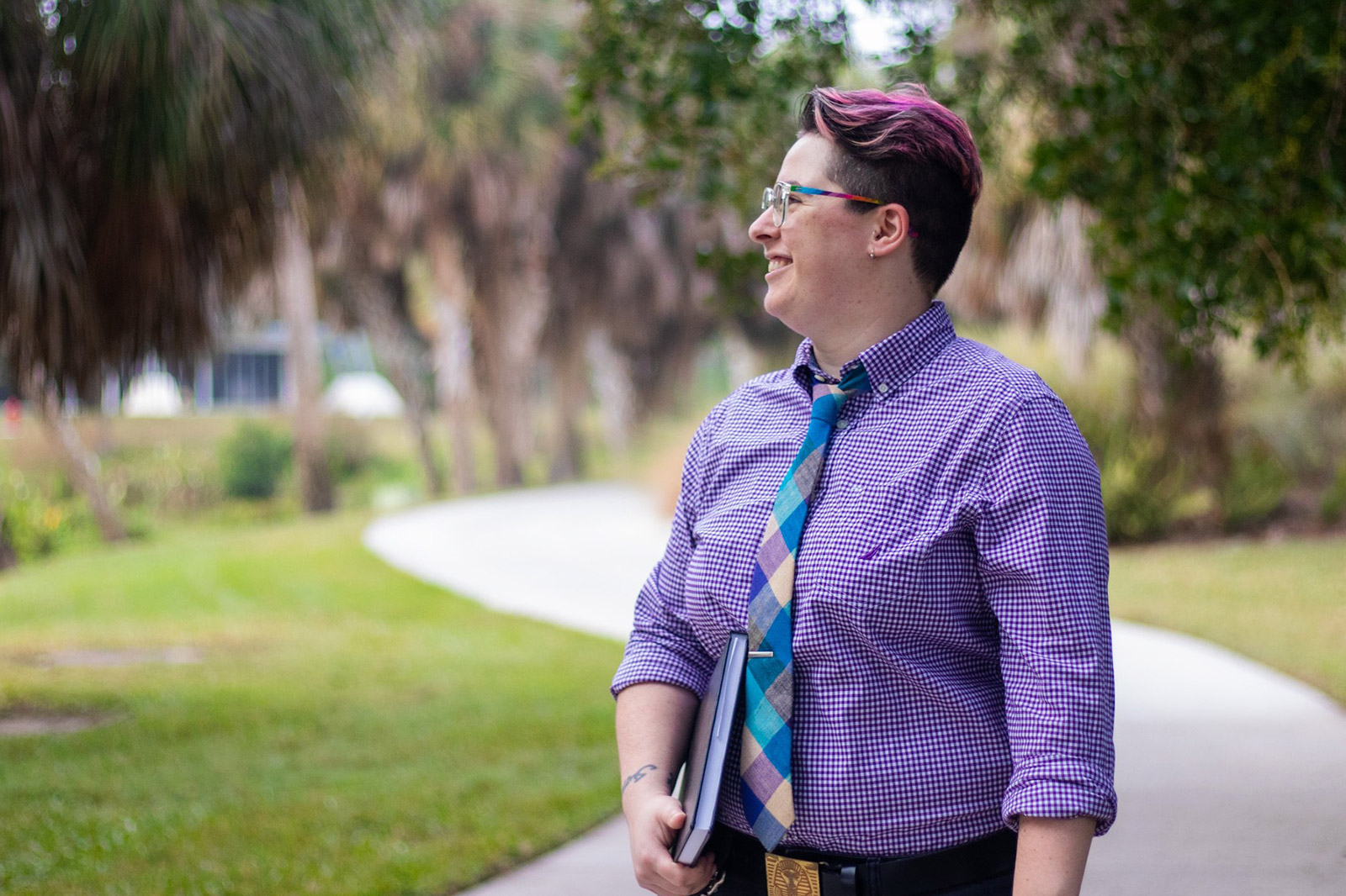 Professor with purple hair and tie on sidewalk on campus