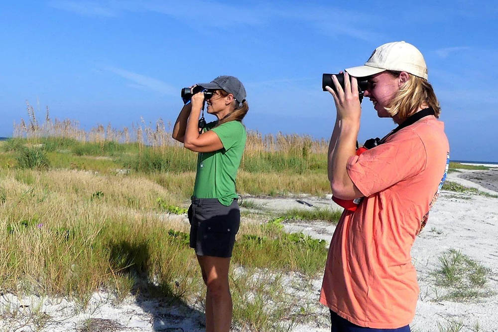 Student and professor looking through binoculars no the beach