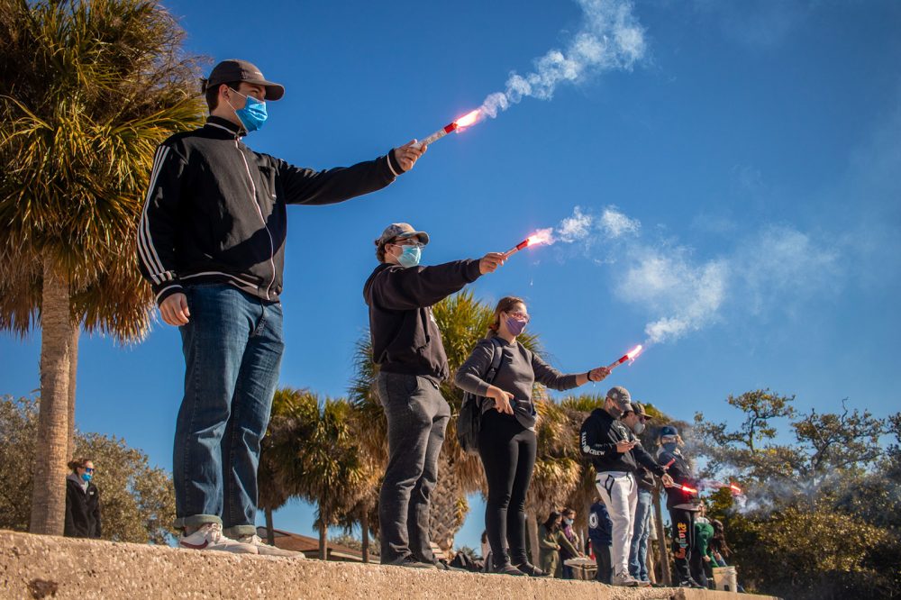 Eckerd students standing on seawall as they light flares