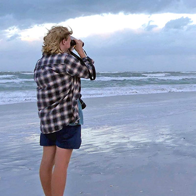 Student looking through binoculars on a rainy beach
