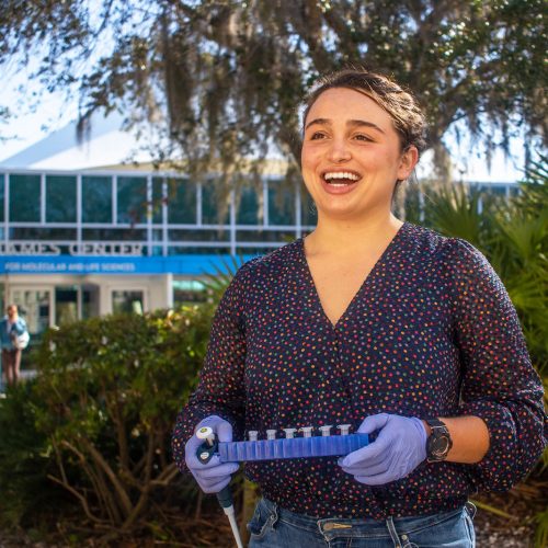 Student wearing gloves and carrying chemistry equipment