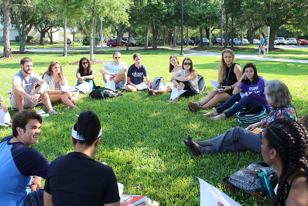 Students seated in a circle in the grass around professor