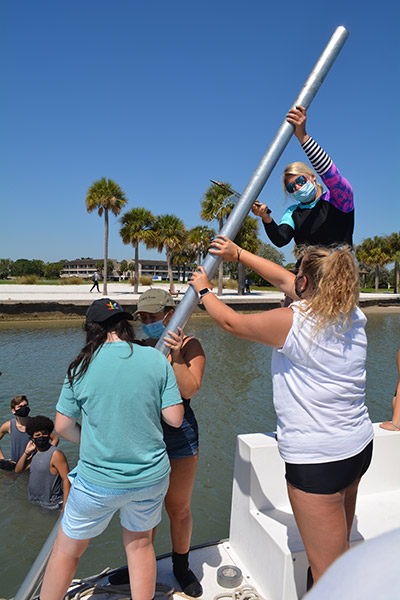 Students hold long metal pole on a boat before placing into the bay