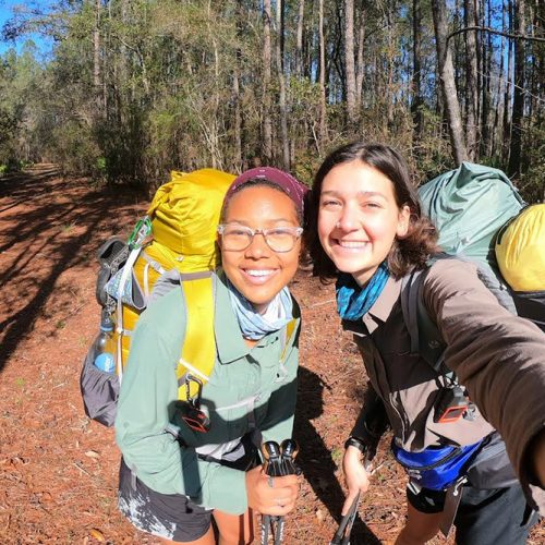 Two Eckerd students wearing backpacks in the woods