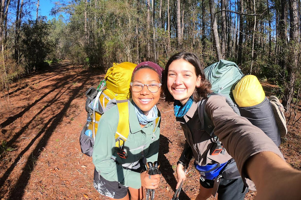Two Eckerd students wearing backpacks in the woods