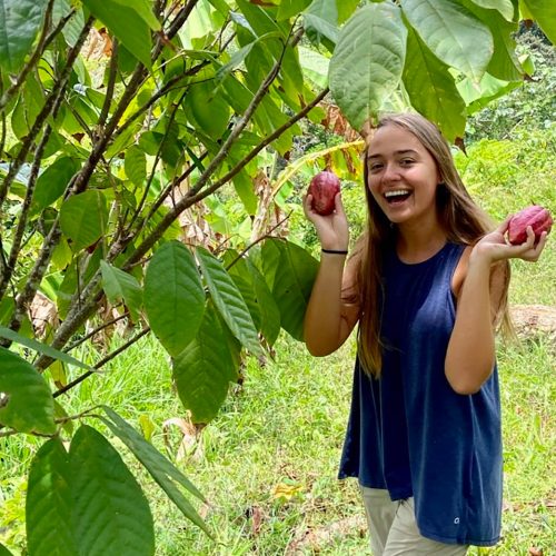 Student holding cacao next to tall plant