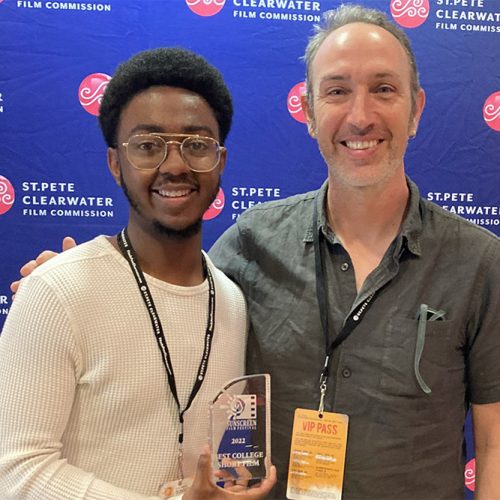 Student holding award stands next to professor in front of a Sunscreen Film Festival screen