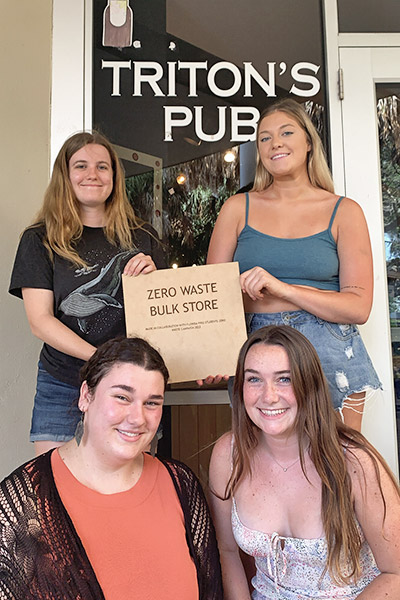 Four students holding a sign that says "Zero Waste Bulk Store" in front of the pub entrance