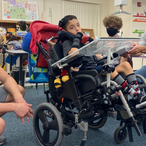 Pupil in a wheelchair with Eckerd students seated around him