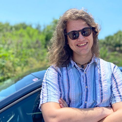 Student standing in front of car, wearing sunglasses