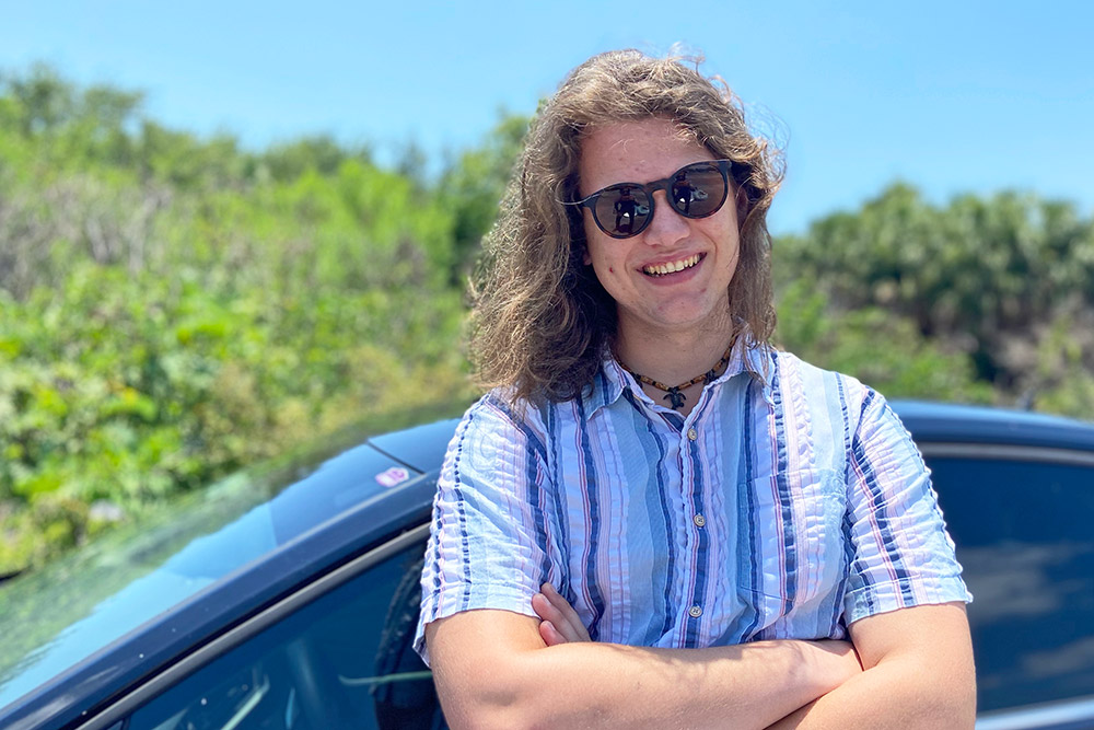 Student standing in front of car, wearing sunglasses