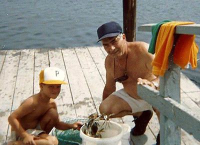 Child holding crab while seated on deck with grandfather