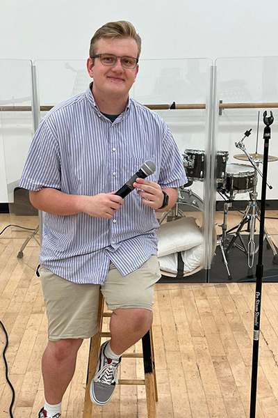 Ryan holding microphone, seated by drum set