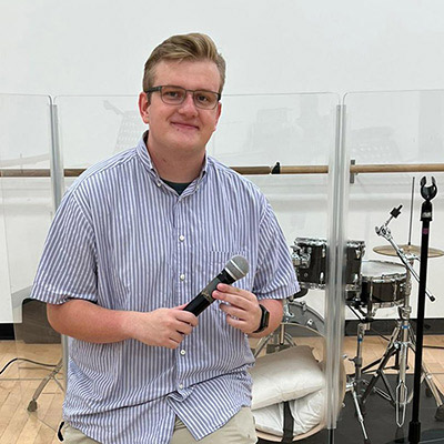 Ryan holding microphone, seated by drum set