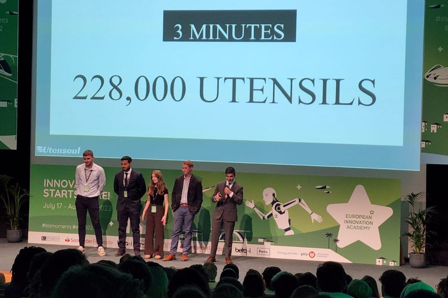 Five students stand on a stage with 228,000 Utensils on screen behind them