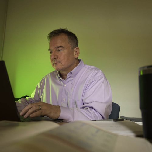 Professor at desk, working on laptop