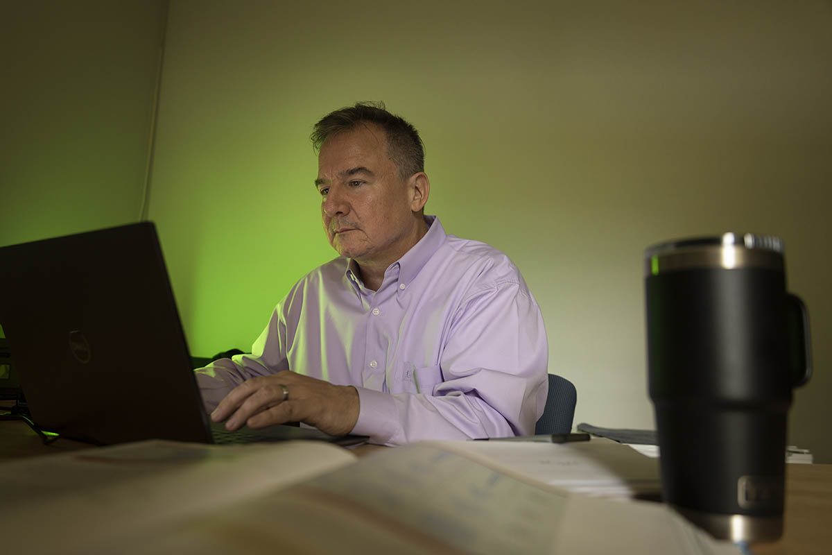 Professor at desk, working on laptop