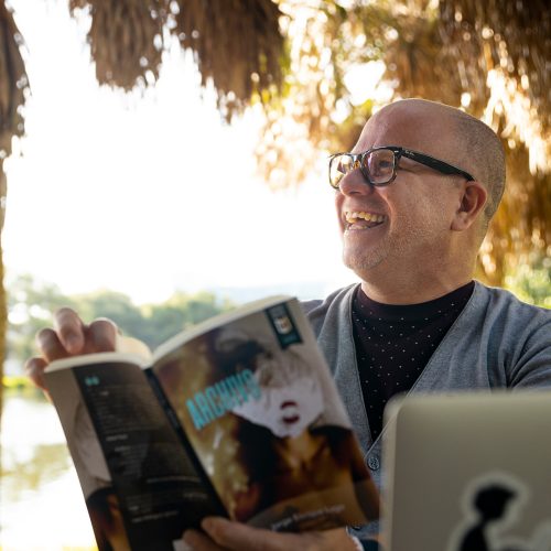 Professor wearing glasses, reading book under chickee by the water