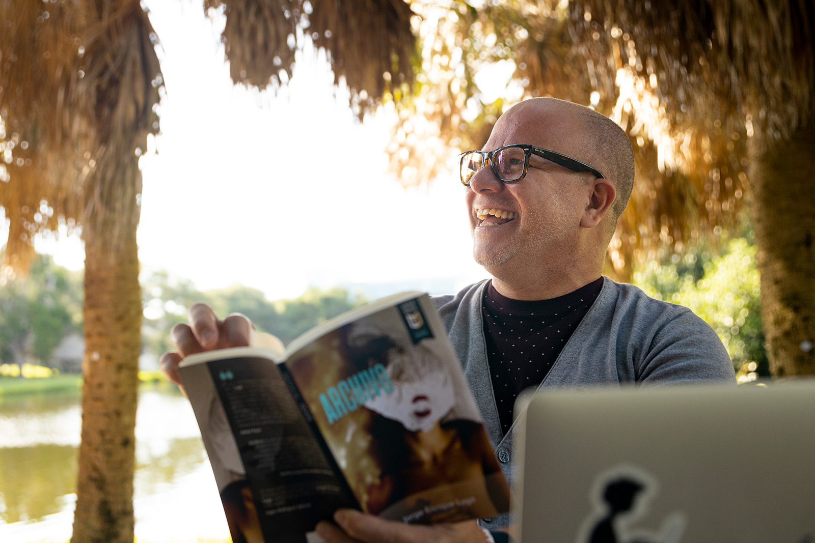 Professor wearing glasses, reading book under chickee by the water