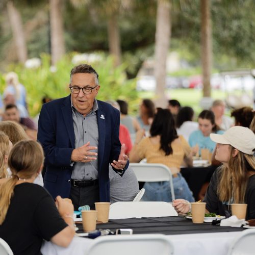 Interim President speaks with students sitting at tables outdoors