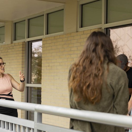 Professor stands along railing while speaking to students