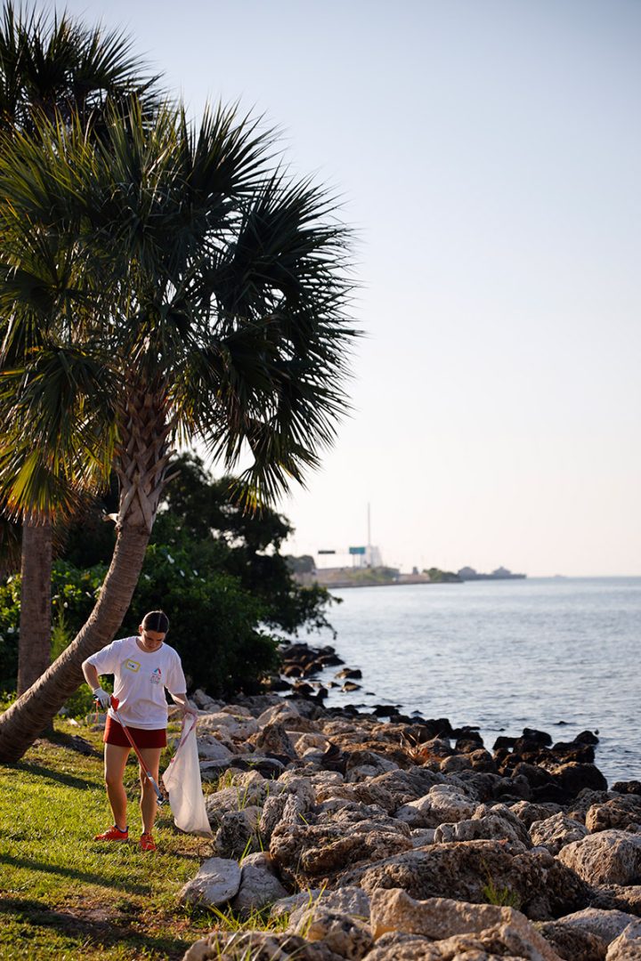 Student picking up trash from rocks along the water