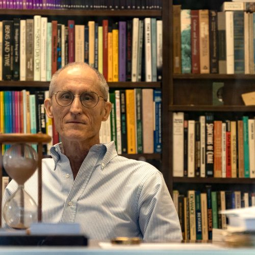 Professor seated in front of books with hourglass in front of him