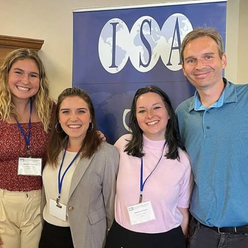 Three students and professor standing before a sign that reads ISA