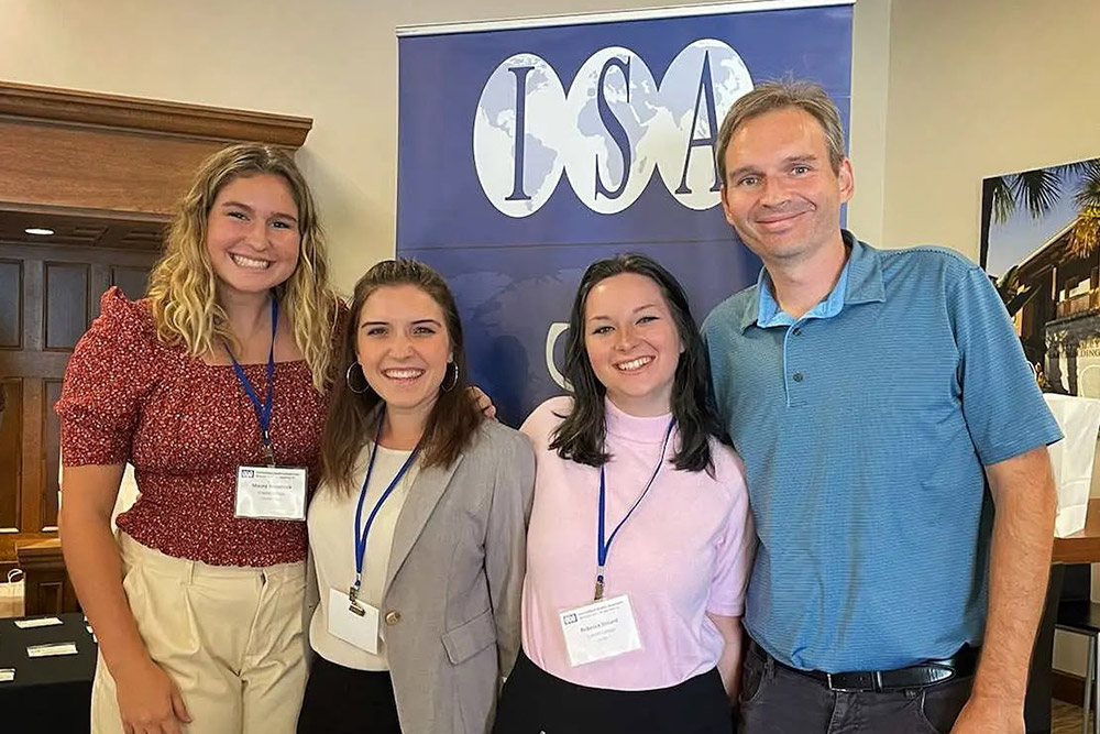 Three students and professor standing before a sign that reads ISA