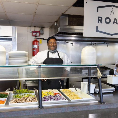 Staff person stands behind food counter with ROAM on sign