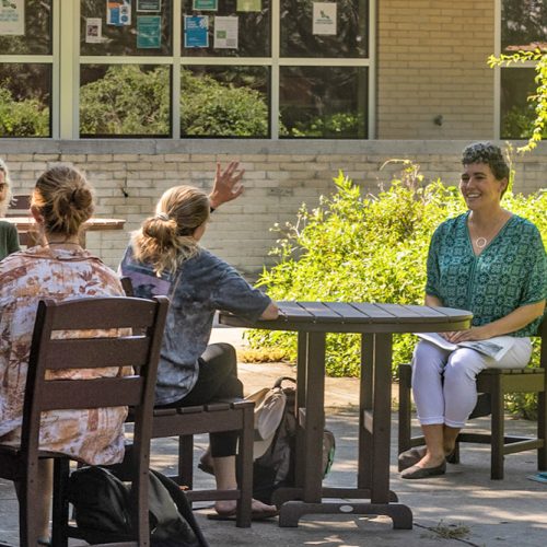 Professor seated outside as a student raises their hand