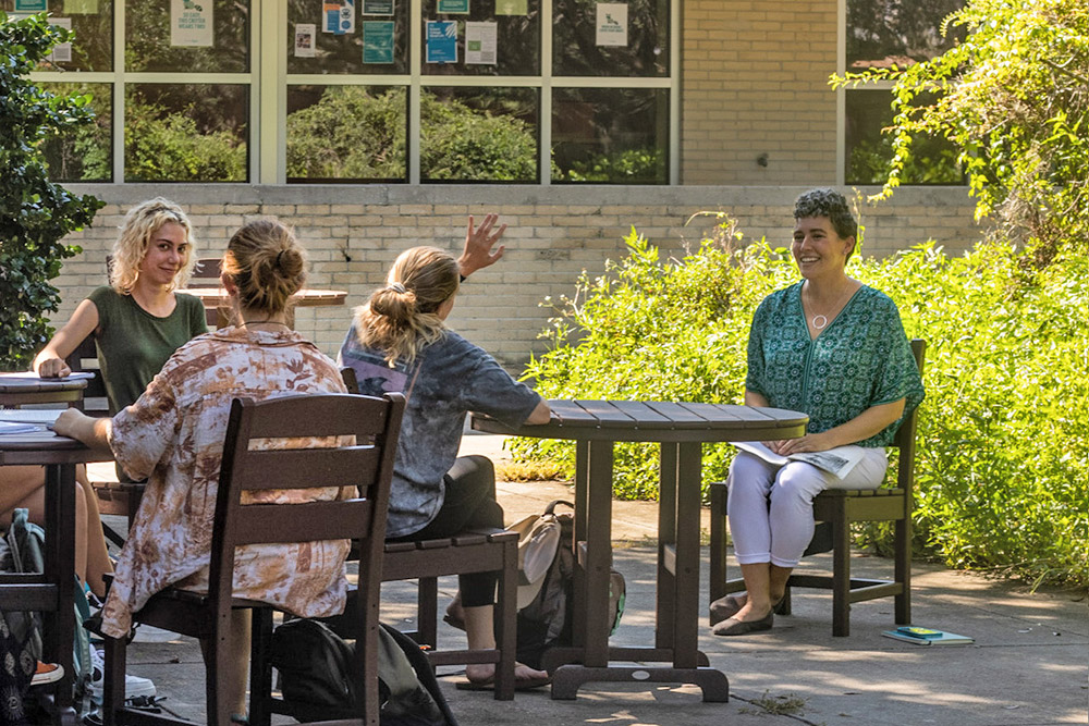 Professor seated outside as a student raises their hand