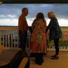 Three people standing on the balcony of Tampa Bay Watch overlooking the water at sunset.