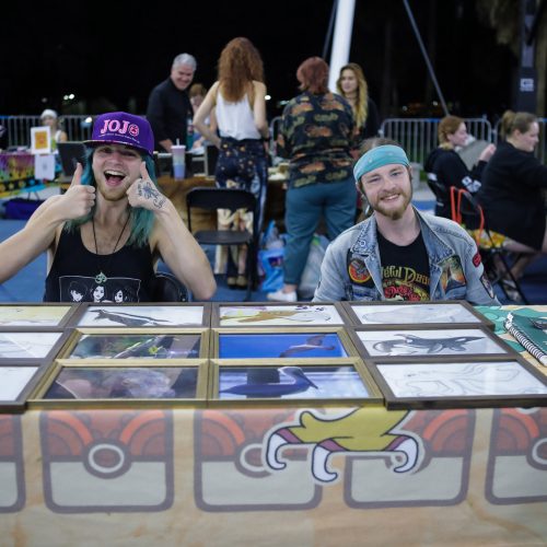 Two students giving thumbs-up sign at a table of art