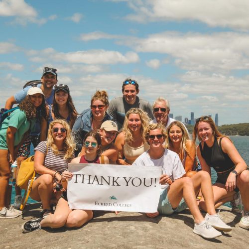 Group of students holding a thank-you banner while posing in front of water