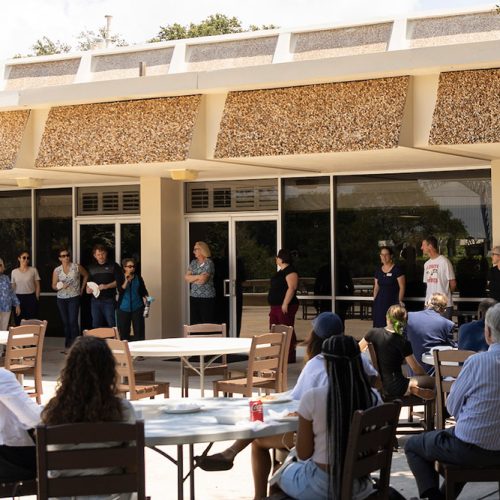 Students seated at tables outdoors listen to speaker