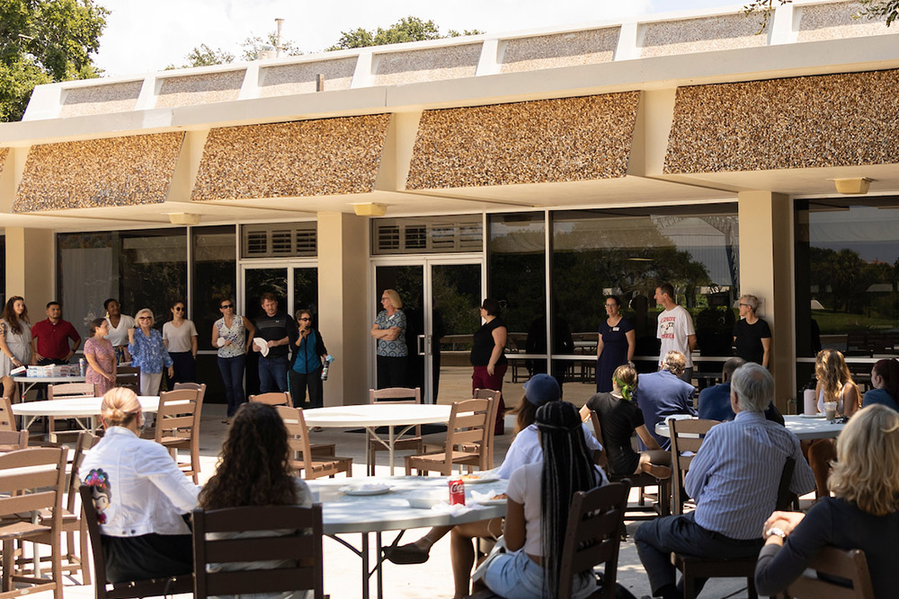 Students seated at tables outdoors listen to speaker