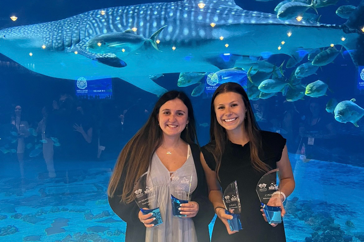 Two students hold trophies in front of whale shark in a tank behind them