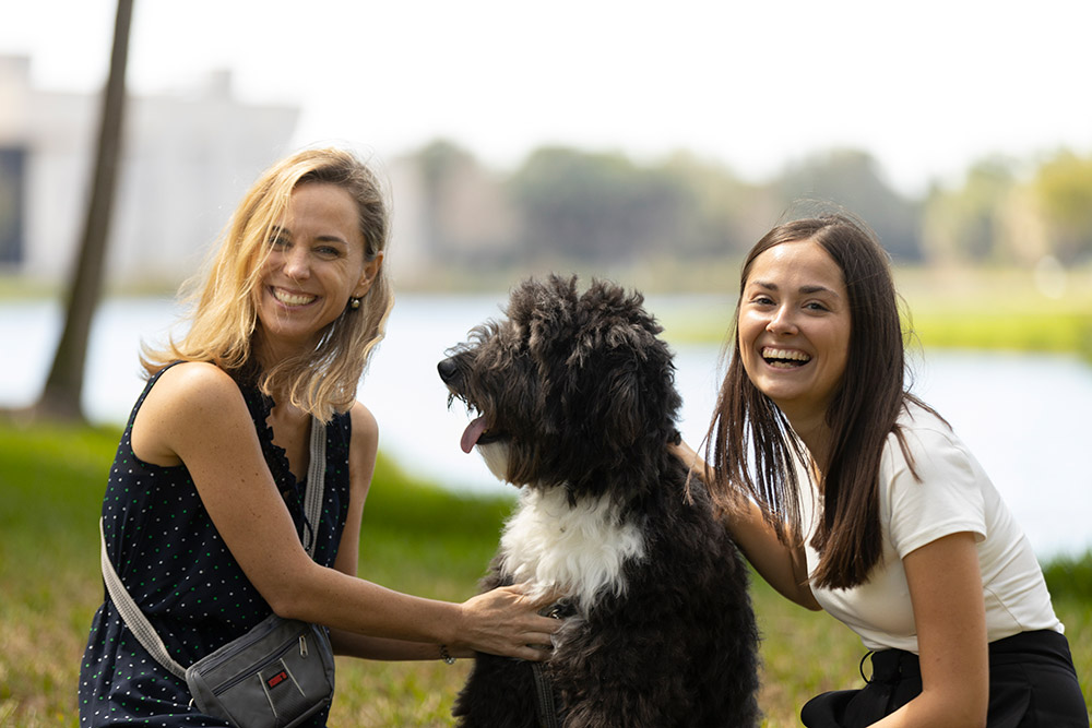 Two women smiling while seated with dog in between them