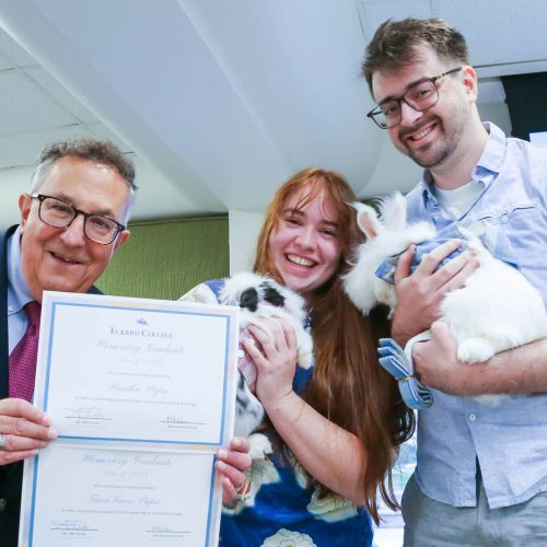 Two students holding bunnies next to president holding their certificates