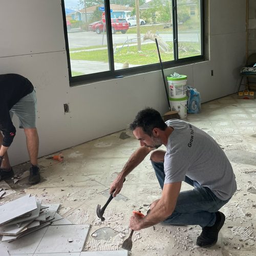 Two volunteers pull up flooring while resident looks out window