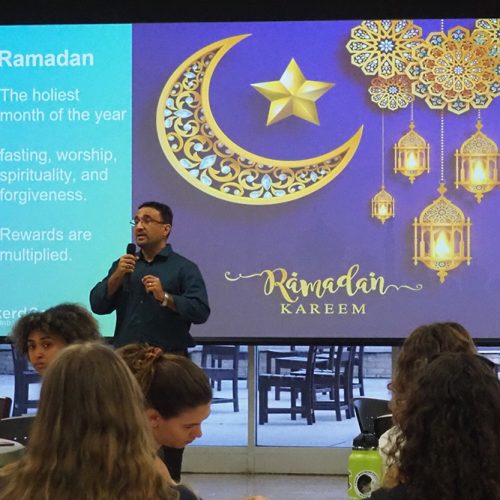 Professor using microphone to speak to an audience with "Ramadan" slide behind him