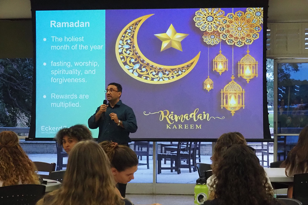 Professor using microphone to speak to an audience with "Ramadan" slide behind him