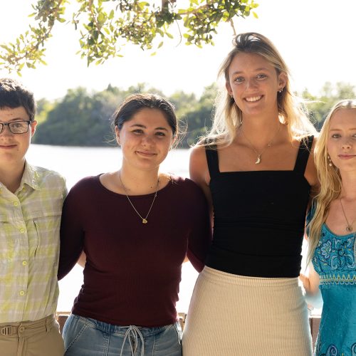 Four students stand side by side in front of pond