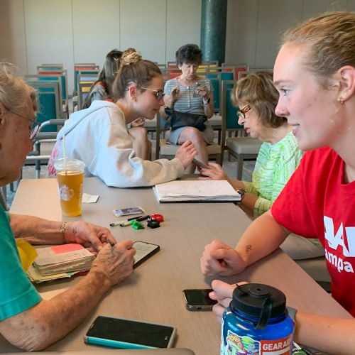 Eckerd students sit at a table with seniors and technological devices