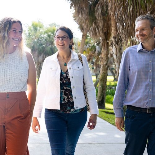 Student walks along path with two professors who are smiling with her