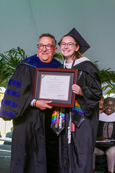 Student in cap and gown and president hold framed certificate